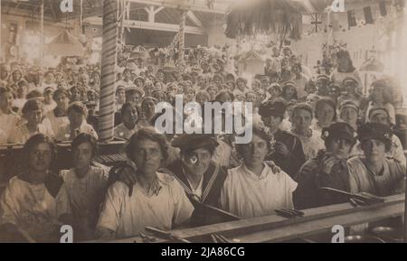 Zigarrenmacher versammelten sich im Zigarrenraum bei W.D. UND H.O. Wills, das Tabakunternehmen in Bristol, am Friedenstag (dem Ende des Ersten Weltkriegs). Das Foto zeigt eine große Gruppe von Frauen, viele junge, die sich hinter ihren Werkbänken versammelt haben. Mehrere sind in Matrosen- und Soldatenuniformen gekleidet und posieren mit Zigarren in den Händen. Auf den Sitzbänken vor ihnen sind auch gerollte Zigarren zu sehen. Der Workshop wurde mit Fahnen der Alliierten, darunter der Union Jack, geschmückt Stockfoto