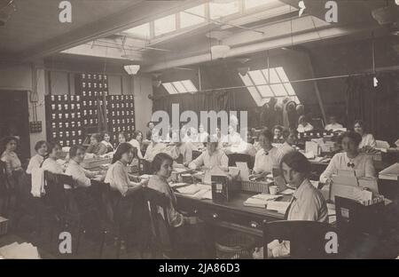 Women's Claims Department, National Health Insurance, Liverpool Victoria Approved Society (LVAS): Büroangestellte sitzen an langen Tischen. Auf den Tischen befinden sich Aktennotizen und Körbe mit Papieren in Aktenschränken. Hüte und Mäntel werden hinten im Büro aufgehängt, teilweise durch einen Vorhang verdeckt. Licht kommt aus einem Dachfenster und schrägen Fenstern in den Dachboden Stockfoto