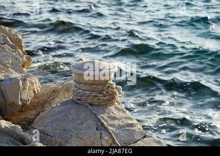Seil, das an einem alten Stock gewickelt wurde, um Boote auf einem Felsen am Meer zu verankern Stockfoto