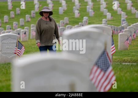 Los Angeles, Kalifornien, USA. 28.. Mai 2022. Eine Frau geht über die Grabsteine, nachdem am Samstag, dem 28. Mai 2022, tausende US-Flaggen auf dem Nationalfriedhof von Los Angeles für die Feierlichkeiten zum Memorial Day in Los Angeles aufgestellt wurden. (Bild: © Ringo Chiu/ZUMA Press Wire) Stockfoto