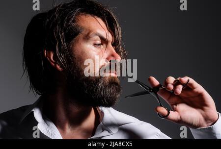 Bärtiger Mann mit Friseurschere. Mans Frisur im Friseur. Bart stylen und schneiden. Barbershop. Stockfoto