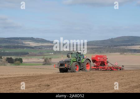 Eine landschaftlich reizende Agrarlandschaft in Aberdeenshire, mit einem Traktor- und Saatbohrer, der in einem gepflügten Feld in Betrieb ist, und Blick über das dahinter liegenden Farmland Stockfoto