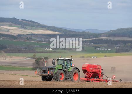 Ein Blick auf die Suie über eine Farmlandschaft in Aberdeenshire, mit einem grünen Fendt-Traktor und einem roten Saatbohrer, der Gerste auf dem nächsten Feld aussaat Stockfoto