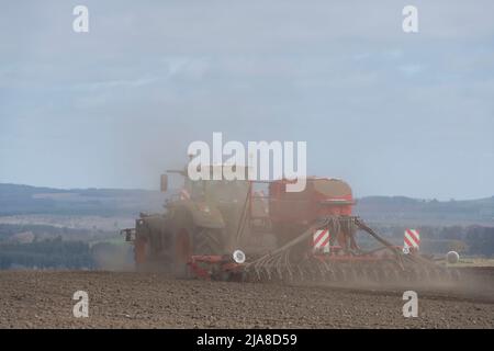 Staubwolken steigen hinter einem roten Horsch-Scheibensaatbohrer auf, der von einem Fendt-Traktor auf einem trockenen gepflügten Feld auf einer schottischen Farm geschleppt wird Stockfoto