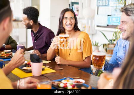 Eine Gruppe lustiger Leute trinkt Bier in einer Bar. 30s Junge Freunde, die Spaß haben und in einer Happy Hour auf dem Dach zu Mittag essen und Alkohol trinken. Stockfoto
