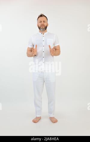 Vertikales Studio schoss einen hübschen Barfußmann, der etwas in weißem Outfit erklärt. Gesunder sportlicher Lebensstil. Speicherplatz kopieren Stockfoto