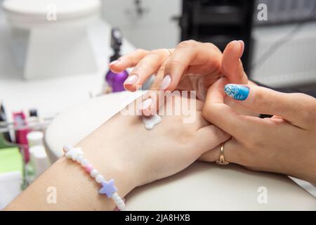 Eine Manikuristin trägt nach einer Hardware-Maniküre in einem Schönheitssalon Handcreme auf weibliche Hände auf. Herz auf die Hand gezogen, Handcreme. Die Creme auf y auftragen Stockfoto