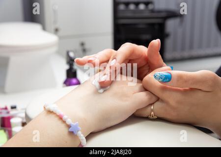 Eine Manikuristin trägt nach einer Hardware-Maniküre in einem Schönheitssalon Handcreme auf weibliche Hände auf. Herz auf die Hand gezogen, Handcreme. Die Creme auf y auftragen Stockfoto