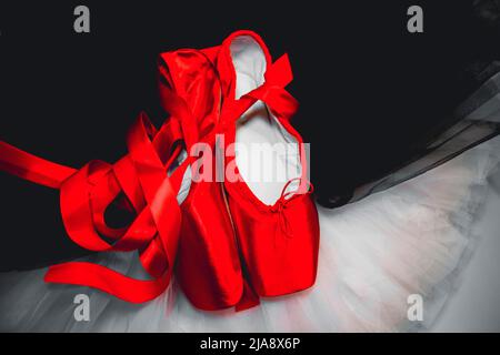 Rote Ballet spitzenschuhe, die auf einem weißen und schwarzen Tutu ruhen. Stockfoto