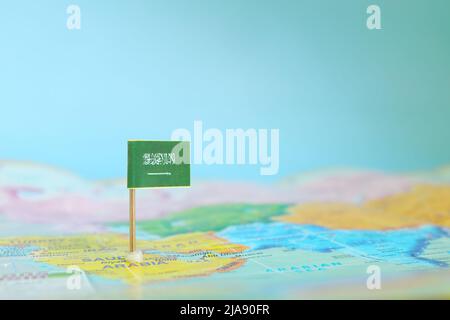 Selektiver Fokus der Saudi-arabischen Flagge auf verschwommener Weltkarte. Standort des Landes. Stockfoto