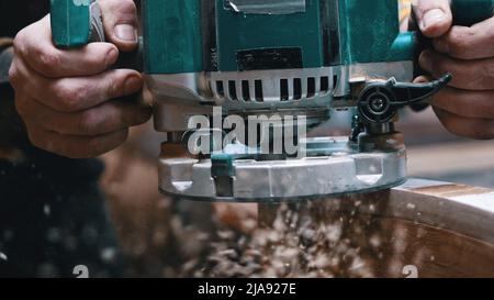 Zimmerei im Innenbereich - ein Holzarbeiter poliert das hölzerne Detail in der Werkstatt - der Staub, der vom Detail wegen des Polierens herabfällt Stockfoto