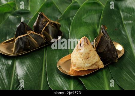 Kue Cang oder Ki Jang und Zongzi oder Bakcang. Chinesische Bohnenkraut klebrig Reisknödel auf grünem Bambus Hinterlassen Hintergrund Stockfoto