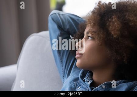 Nachdenkliches Mädchen mit natürlichen lockigen Haaren, die auf der Couch zu Hause ruhen Stockfoto