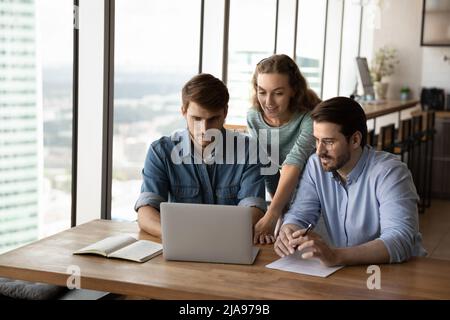 Fokussierte kreative Gruppe, die gemeinsam virtuelle Präsentationen auf einem Laptop ansieht Stockfoto