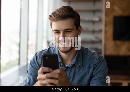 Glücklicher Tausendjähriger Kerl mit Smartphone, Lesen, SMS, Lächeln auf dem Bildschirm Stockfoto