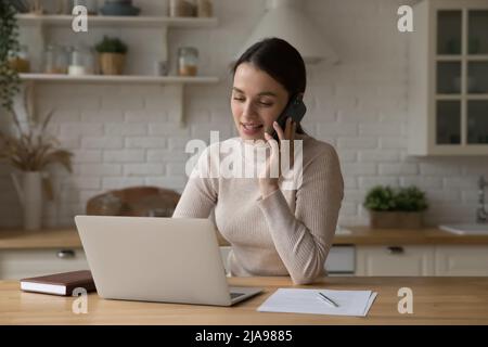 Positiv engagierte junge freiberufliche Frau, die in der Küche zu Hause arbeitet Stockfoto