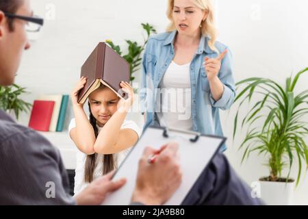 Hand eines professionellen Familien-Psychotherapeuten, der während einer Konsultation Notizen vor einer Familie mit einem Kind schreibt Stockfoto