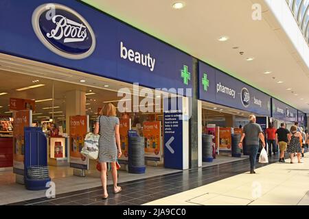 Green Pharmacy Cross-Schilder über den Eingängen zu Boots Chemiker Einzelhandel Geschäft & Beauty-Shop Käufer in Einkaufszentrum Mall Chelmsford England Großbritannien Stockfoto