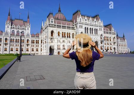 Urlaub in Budapest. Rückansicht von schönen stilvollen Mädchen genießen Blick auf das ungarische Parlamentsgebäude in Budapest, Ungarn. Tourismus in Europa. Stockfoto