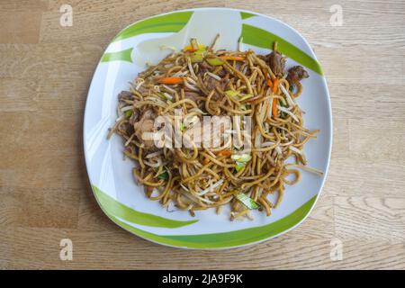 Chinesische gebratene Nudeln mit Hühnerfleisch, Gemüse und Sauce auf einem Teller und einem Holztisch, Kopierraum, Hochwinkelansicht von oben, ausgewählter Fokus Stockfoto