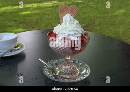 Eisbecher mit Erdbeeren und Schlagsahne in einer Glasschüssel auf einem Tisch im Gartencafé serviert, Kopierraum, ausgewählter Fokus, enge Tiefe Stockfoto