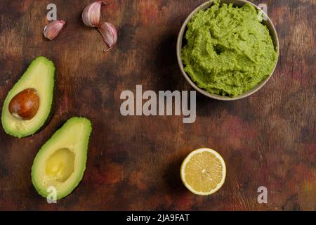 Traditionelle lateinamerikanische mexikanische Sauce Guacamole in Tonschüssel, schneiden Sie halbe Avocado- und Avocado-Sandwiches auf dunklem Hintergrund. Draufsicht Stockfoto