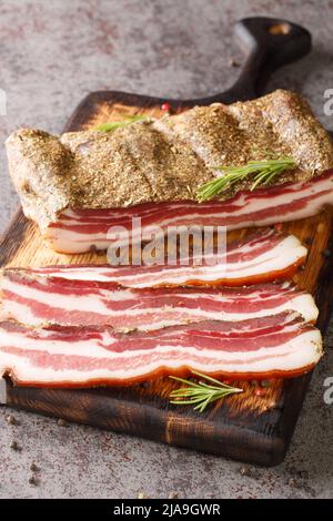 Geräuchertes italienisches Pancetta-Fleisch aus der Nähe auf dem Holzbrett auf dem Tisch. Vertikal Stockfoto