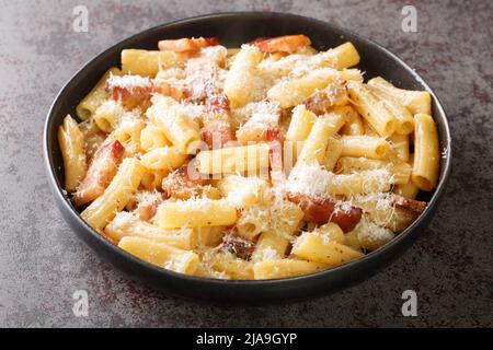 Italienische Pasta alla Gricia auf einem Teller mit geriebenem Pecorino romano und guanciale aus der Nähe auf dem Tisch. Horizontal Stockfoto