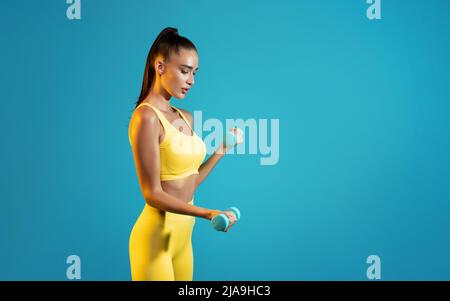 Seitenansicht Fitness Lady Training Mit Hanteln, Blauer Hintergrund Stockfoto