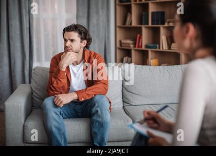 Der junge kaukasische Mann will nicht mit einem Psychiater im modernen Klinikinneren sprechen Stockfoto