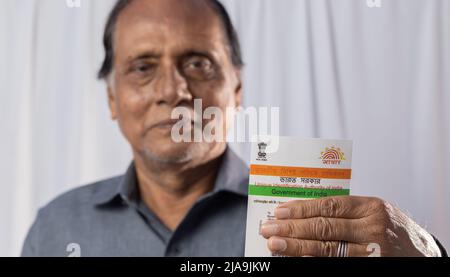 Birbhum, Westbengalen / Indien - 15. März 2022: Selektiver Fokus auf die Aadhaar-Karte, die von einem alten indischen Mann mit lächelndem Gesicht in der Hand gehalten wird Stockfoto