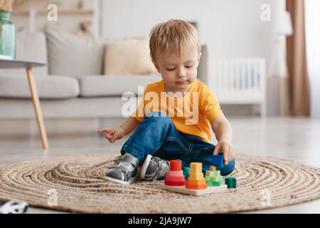 Frühzeitiges Entwicklungskonzept. Kleiner Kleinkind Junge spielt mit pädagogischem Holzspielzeug zu Hause, sitzt im Wohnzimmer Stockfoto