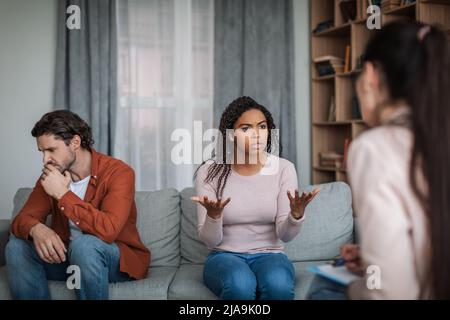 Wütend unzufrieden junge schwarze Frau sprechen mit Psychologe, ignorieren europäischen Ehemann in der Klinik Stockfoto