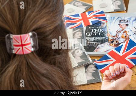 Fan von Queen Elizabeth mit königlichen Erinnerungsstücken auf einem Tisch, darunter Münzen der Royal Mint, britische Flaggen und das OK Magazine - bereit für das Platin-Jubiläum Stockfoto