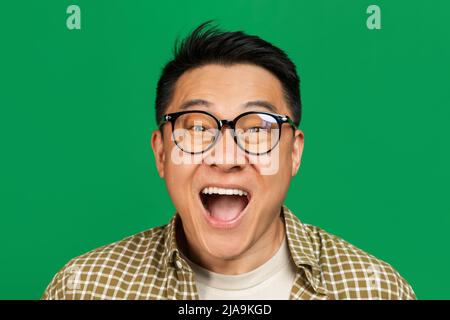 Leistungskonzept. Emotionaler reifer asiatischer Mann, der jubelt und schreit und den Sieg über grünen Hintergrund feiert Stockfoto