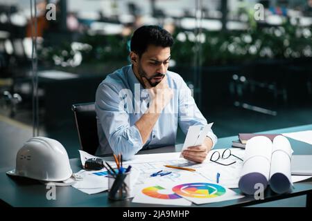 Nachdenkliche Millennial islamischen männlichen Ingenieur in Brille mit Bart denken an Farbe für Projekt am Arbeitsplatz Stockfoto