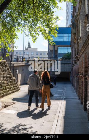 Zwei junge Menschen gehen an einem sonnigen Tag in Newcastle upon Tyne, Großbritannien, durch die Stadt, vorbei am Holy Jesus Hospital. Stockfoto