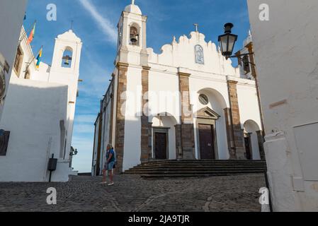 Weibliche Touristen, die an der Pfarrkirche von Nossa Senhora da Lagoa in Monsaraz, Alentejo, Portugal, vorbeigehen. Stockfoto