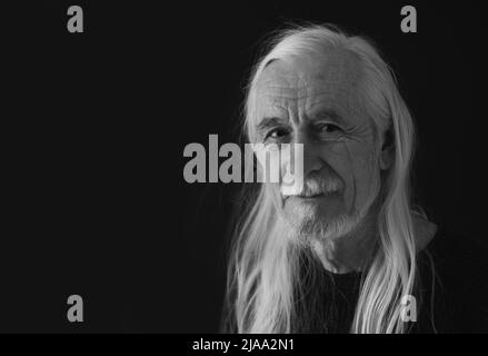 Low-Key Studio schwarz-weiß Porträt von lächelnden attraktiven alten Mann mit losen langen grauen Haaren. Horizontal. Stockfoto