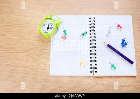 Notizblock mit violettem Stift, Papier, Clips und Wecker auf dem Schreibtisch Stockfoto