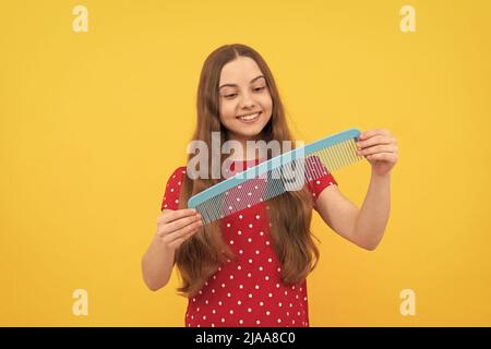 Happy Kid Bürsten lange Haare mit Kamm auf gelbem Hintergrund, Haarpflege Stockfoto