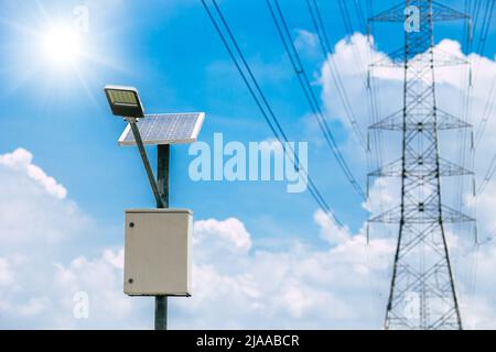 Solarpanel-Lampe mit Hochspannungsturm auf blauem Himmel Hintergrund für nachhaltige Energie Stockfoto