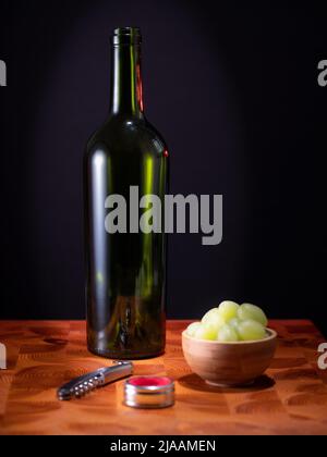 Helsinki / Finnland - 29. MAI 2022: Eine leere Rotweinflasche, ein Glas Wein und einige Trauben auf einer Holzfläche vor dunklem Hintergrund. Stockfoto