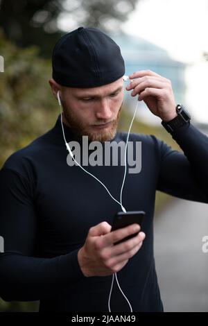Nahaufnahme der jungen weißen Mann mit Bart, Kopfhörer im Ohr. Bestimmt Sportler ist bereit für lange Strecken laufen und Training Athlet Verschleiß Stockfoto