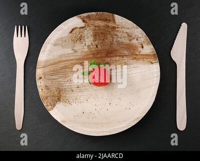 Palmblattplatte mit einzelnen Erdbeer- und Holzbesteck auf schwarzer Schiefertafel, Ökologie und Zero Waste Konzept, Draufsicht Stockfoto