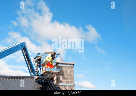 Bauherren, die vom Teleskopausleger-Lift aus arbeiten, montieren wärmegedämmte Sandwichpaneele an der Fassade eines neuen mehrstöckigen Wohngebäudes. Wo Stockfoto