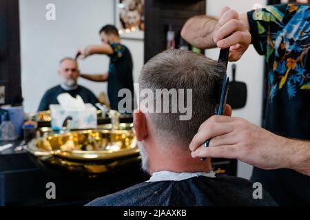 Ein alter Mann, der in einem Friseurladen einen Haarschnitt von einem Meister genießt. Ein alter Mann bekommt einen stylischen Haarschnitt Stockfoto