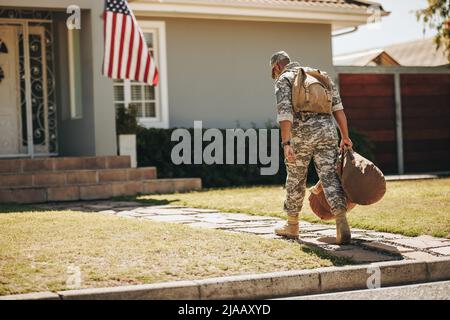 Patriotischer junger Soldat, der mit seinem Gepäck auf sein Haus zugeht. Rückansicht eines mutigen amerikanischen Militäranmannes, der nach seinem Dienst nach Hause kam Stockfoto