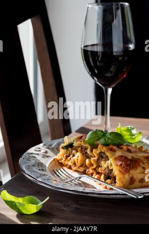 Gourmet Lasagne Roll Ups serviert mit Rotwein vor einem sonnigen Fenster. Stockfoto