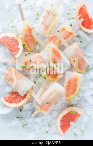 Ein Haufen erfrischender eisiger, kalter Grapefruit-Thymianpopsicles auf Eiswürfeln. Stockfoto